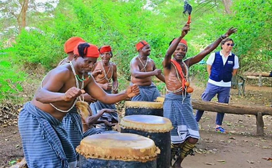 Dawida dancers in red caps and beadwork performing the Mwazindika dance around large drums.